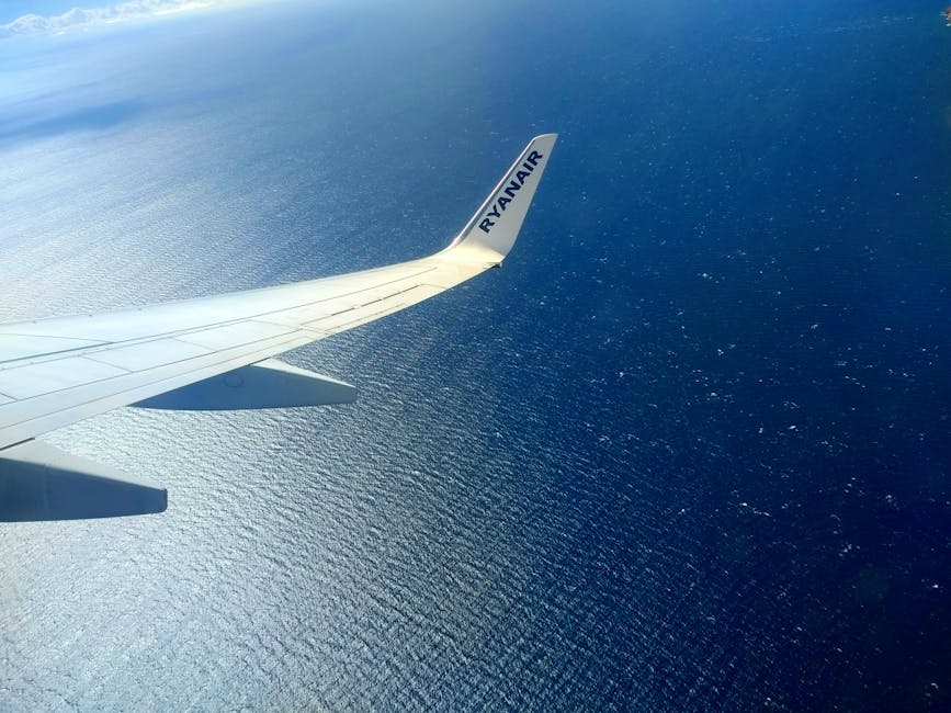Aerial photo of a Ryanair wing flying over the ocean under bright daylight.